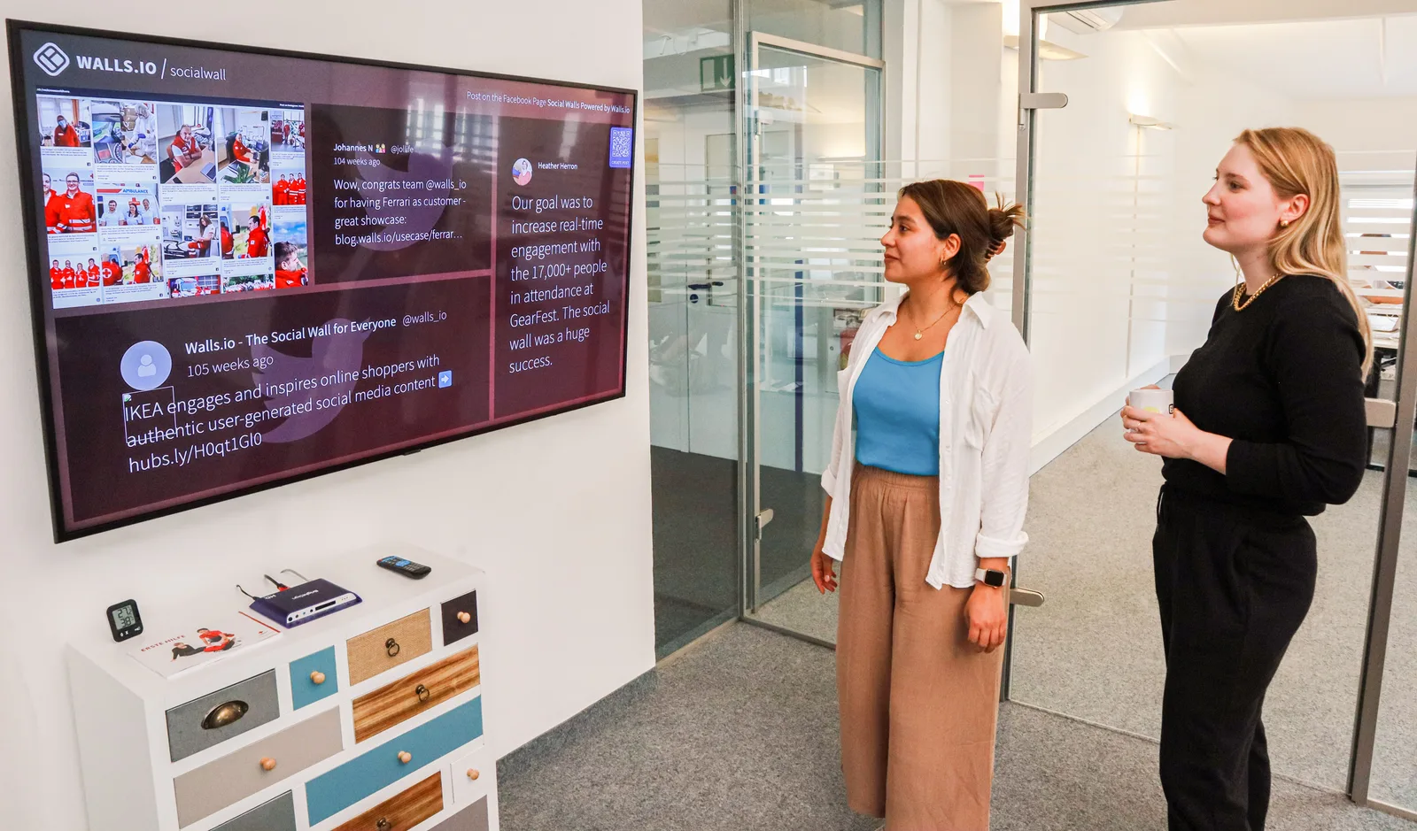 Two women engage with a digital presentation on a screen in a modern office setting. Which social media content planning agencies to pick