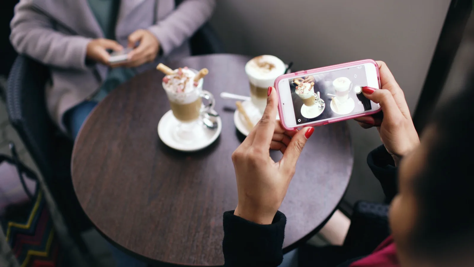 Two women in a cafe capturing photos of their coffee with smartphones. Which social media strategy questions come first