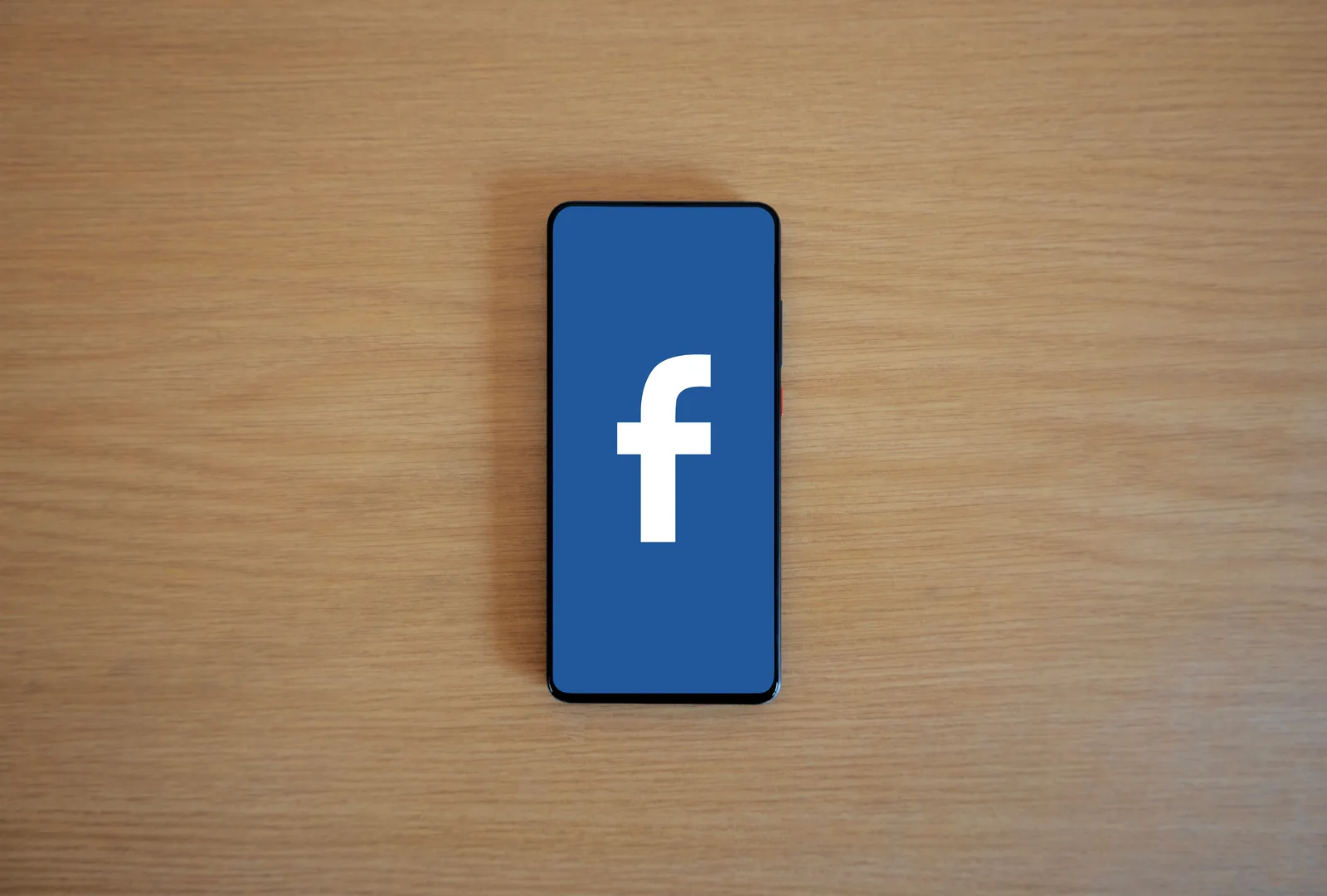 Smartphone with Facebook logo on screen, placed on a wooden background. Top view. Facebook ads versus boosted posts for Canadian small businesses