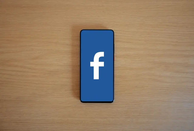 Smartphone with Facebook logo on screen, placed on a wooden background. Top view. Facebook ads versus boosted posts for Canadian small businesses