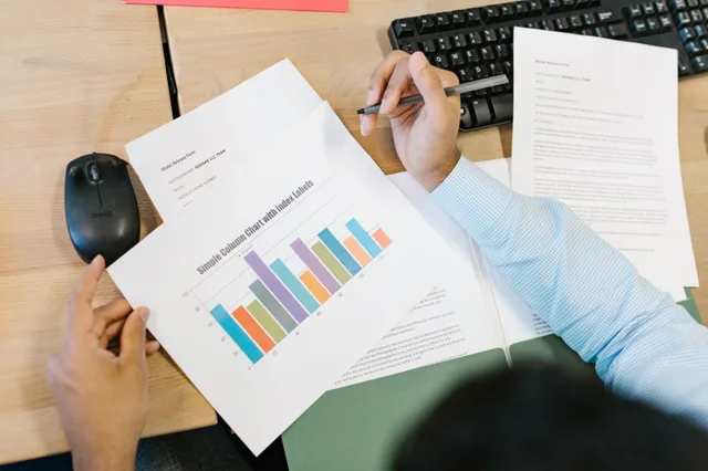 A business analyst reviews a colorful bar chart and documents at a desk, indicating data analysis. How to build influencer campaign management benchmarks