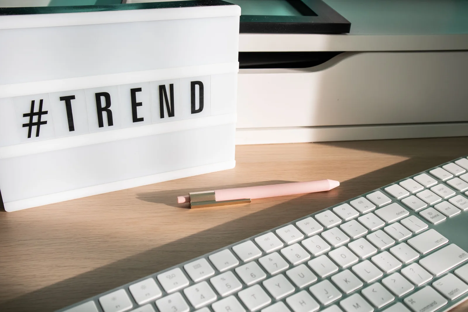 Contemporary workspace featuring a light box showing '#trend,' a pink pen, and a keyboard. Content planning in the AI era: more drafts, more review, less certainty
