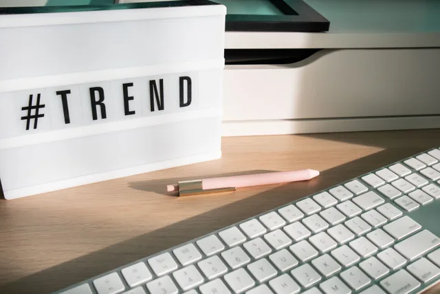 Contemporary workspace featuring a light box showing '#trend,' a pink pen, and a keyboard. Content planning in the AI era: more drafts, more review, less certainty