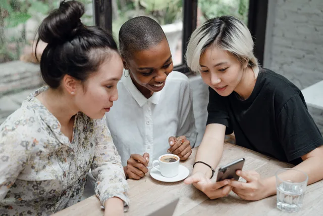 From above of young multiracial female colleagues discussing project and using smartphone in creative coworking space. Social media strategy best practices for business teams