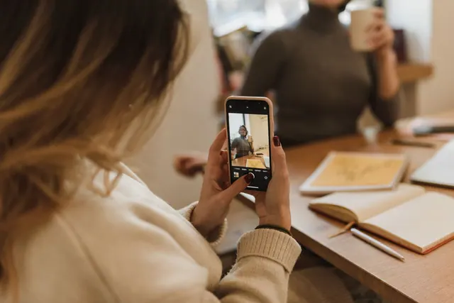 Woman captures a relaxed office moment with smartphone, emphasizing social media and small business. Reach versus real outcomes: the costliest strategy mistake teams make